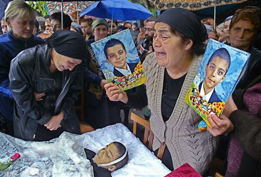 Fedosya Beroyeva, grand mother of 10-year old twins, Soslan, right, and Aslan, killed in the school hostage taking, cries holding their portraits as their mother Zalina, left, looks at Aslan's body during the twins' funeral in Beslan, Monday Sept. 6, 2004. (AP)